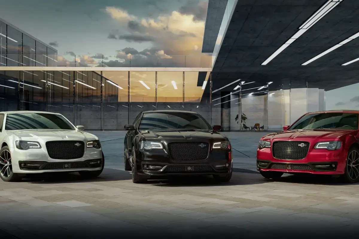 Three Chrysler 300 sedans in white, black, and red parked in front of a modern glass building at sunset.