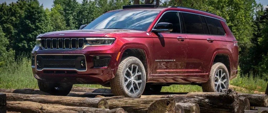 Red Jeep Grand Cherokee L SUV parked on log bridge surrounded by forest