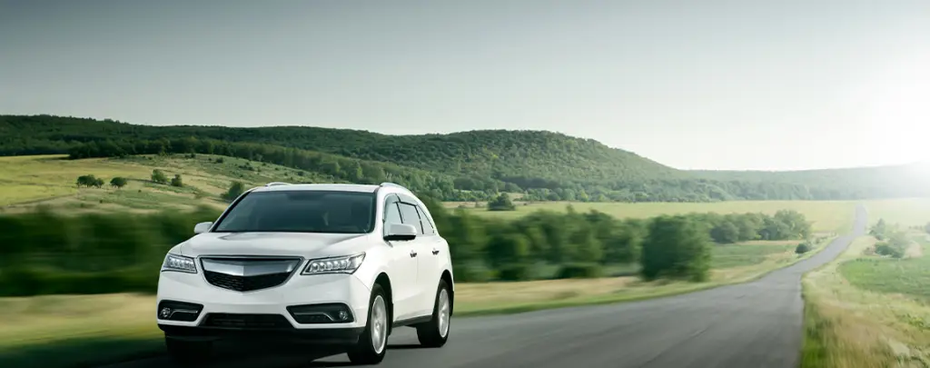 White Acura MDX SUV driving on rural road through green rolling hills