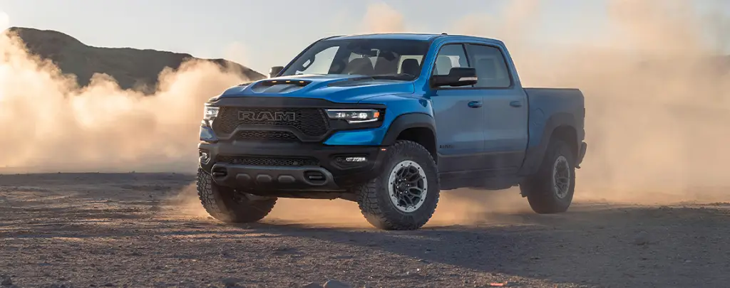 Blue Ram 1500 TRX pickup truck kicking up dust driving through desert terrain
