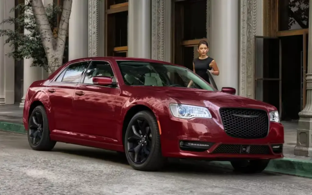 Red Chrysler 300 sedan parked on city street with woman entering building